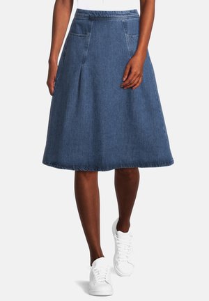 Jupe trapèze en denim avec poches avant, portée avec des baskets blanches et un haut blanc, visible de la taille jusqu'au milieu du mollet.