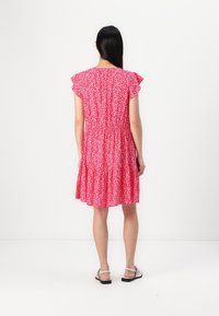 Rotes Blumenkleid mit kurzen, Rüschenärmeln, geschnürter Taille und stufigem Saum. Der Stoff zeigt ein Muster aus kleinen weißen Blumen. Kombiniert mit Riemchensandalen.