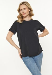 Sort kortærmet t-shirt med opsmøg, lavet af blødt stof, kombineret med lyseblå jeans, præsenteret mod en hvid baggrund.