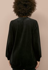 Top negro de manga larga en suave tela aterciopelada con escote redondeado. Presenta un corte holgado y puños ligeramente fruncidos.