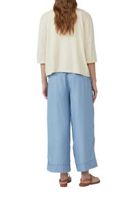Top corto a maniche corte color beige chiaro e pantaloni ampi blu chiaro. Il top ha una vestibilità rilassata; i pantaloni presentano orli ripiegati e una texture morbida.