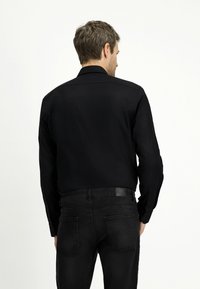 Camicia nera con colletto classico, maniche lunghe e texture liscia, abbinata a jeans in denim scuro con design a cinque tasche.