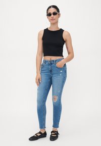 Black crop top, light blue ripped skinny jeans with frayed hems, and black flats with strap details. Simple design, casual fit.