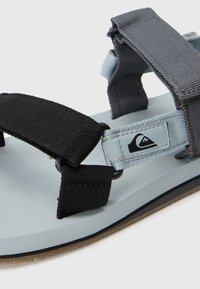 Sandale ajustable noire et bleu clair avec des sangles robustes, un semelle intérieure texturée et une semelle foncée contrastante avec un détail de logo.
