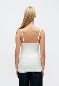 Hvit ribbestrikket singlet med justerbare stropper og blonderkant nederst, med en tettsittende passform og glatt tekstur.