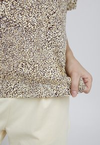 Leopardmönstrad kortärmad topp i beige och bruna toner, tillverkad av mjukt tyg som faller lätt, kombinerad med ljusa byxor.