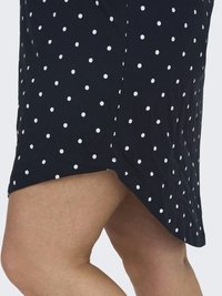 Falda de lunares azul marino con lunares blancos, confeccionada en un tejido suave. Presenta una abertura lateral y un dobladillo que se curva hacia arriba en los laterales.