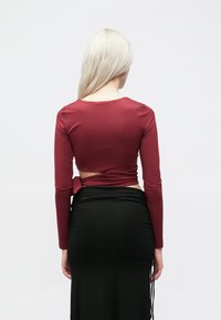 Dugi rukav maroon majica s izrezom na leđima, u kombinaciji s prilagođenom crnom suknjom koja ima nabranu tkaninu i bočne kravate.