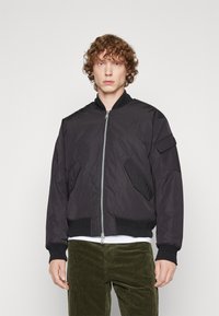 Giacca bomber nera con chiusura a zip, polsini e orlo a costine, due tasche laterali e un logo discreto sul petto. Tessuto morbido.