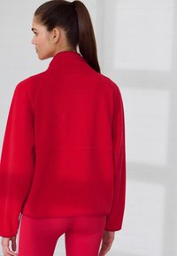 Rode fleece jas met een hoge kraag, lange mouwen en een relaxte pasvorm. Heeft naaddetails en een gladde textuur.