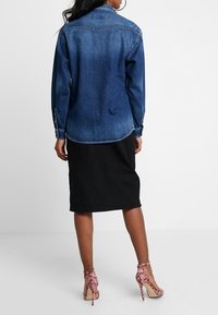 Veste en denim, bleue, avec des manches longues, des poignets boutonnés, un col pointu et une coupe droite. Assortie à une jupe noire jusqu'aux genoux et des talons roses.