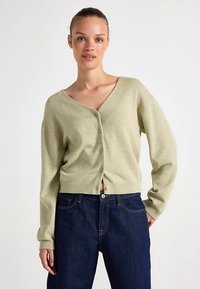 Light green short cardigan with a deep V-neck, five buttons down the front, and ribbed cuffs. Worn over dark blue jeans.