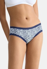 Katoenen slips met een wit en marineblauw patroon, voorzien van kant langs de tailleband. De stof heeft een zachte textuur.