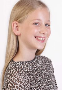 Kind met een luipaardprint top met een ronde hals en korte mouwen, met kleine gouden oorbellen met gekleurde stenen, lachend.