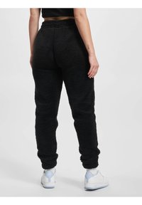 Svarte fleece joggebukser med en teksturert overflate, elastisk livlinning og smale ankler. Sammen med hvite sneakers med lys blå detaljer.