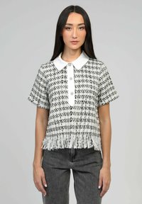 Haut à manches courtes texturé noir et blanc avec un col blanc, des boutons sur le devant et un ourlet à franges.