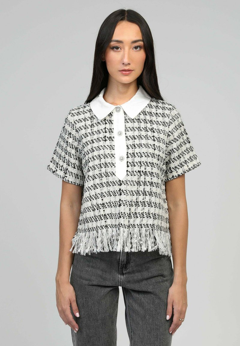 Haut à manches courtes texturé noir et blanc avec un col blanc, des boutons sur le devant et un ourlet à franges.