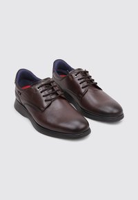 Zapatos de cuero marrón con un acabado suave, que presentan una puntera redondeada, un diseño de cordones, un forro interior azul oscuro y suela de goma.