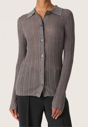 Cardigan gris à manches longues en maille côtelée avec boutons, porté sur un pantalon noir, présenté sur une personne debout du cou aux hanches.
