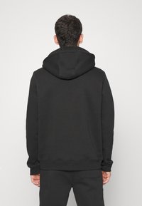 Zwarte sweatshirt met capuchon, met een ontspannen pasvorm, zachte textuur en geribbelde boorden en onderkant. Achteraanzicht toont een gladde afwerking en een minimalistisch ontwerp.
