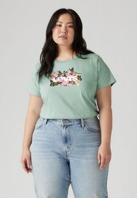 Mint green t-shirt with short sleeves and floral graphic print in pink and black, paired with high-waisted light blue denim jeans.
