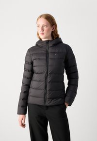 Black puffer jacket with a zip front, hood, and horizontal quilted texture. Features a small logo on the chest and elastic cuffs.