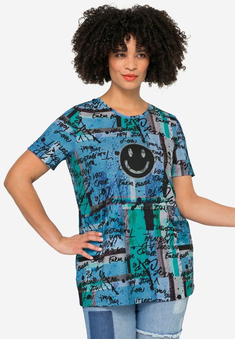 T-shirt décontracté multicolore présentant différentes nuances de bleu et de vert, avec un graphique de visage souriant et des motifs de texte manuscrit. Matière en mélange de coton.