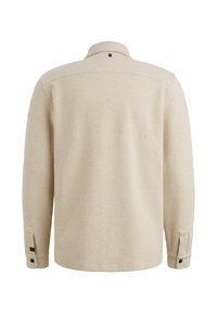 Beżowa koszula z długim rękawem o teksturowanym wzorze waflowym, z zapięciem na guziki przy mankietach i kołnierzem zakładanym, z małym detalem metki na plecach.