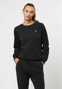 Svart sweatshirt i mjukt tyg med rund halsringning, långa ärmar och en liten logotyp på bröstet. Avslappnad, ledig passform.
