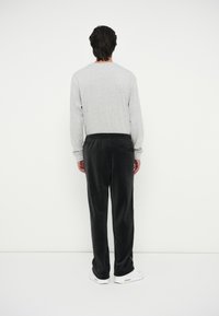 Pilka ilgos rankovės marškiniai derinami su juodais veliūro kelnais. Apranga pasižymi atsipalaidavusiu siluetu ir subtilia mėlyna akcentu ant kelnių.