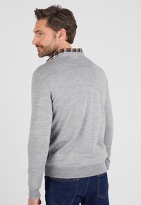 Maglione grigio lavorato a maglia con scollo rotondo e polsini a costine, indossato sopra una camicia a quadri. Tessuto liscio, materiale leggero, design aderente.