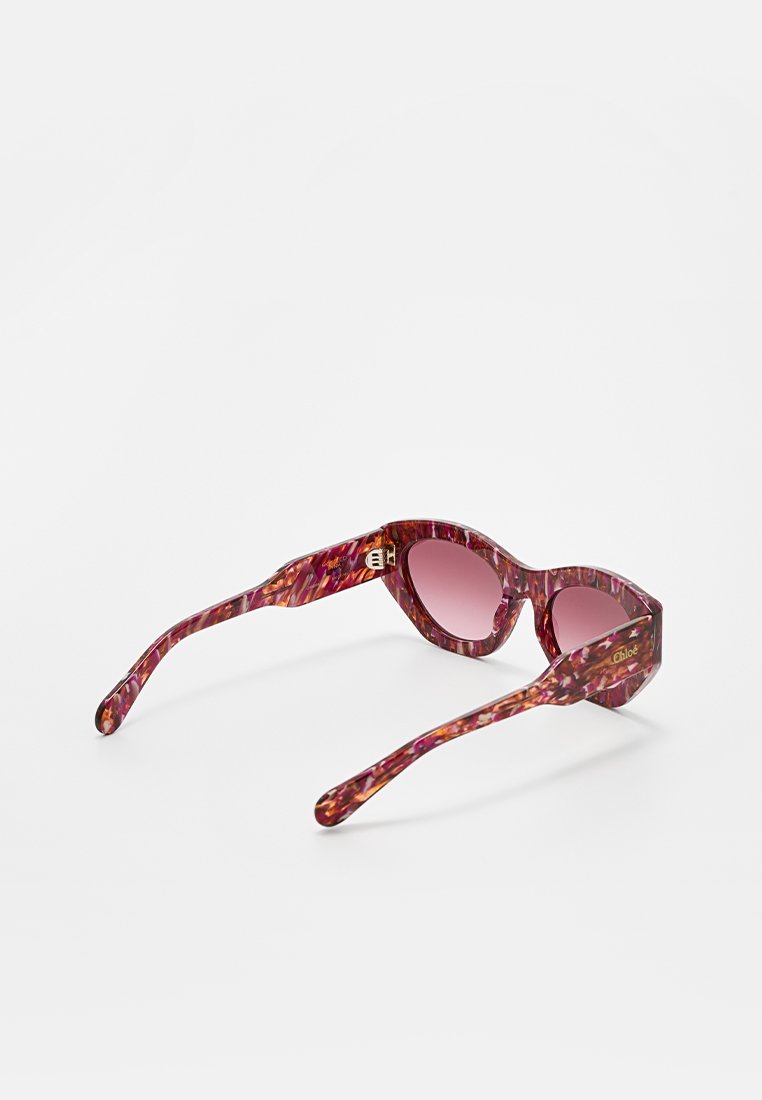 Okulary przeciwsłoneczne z owalnymi różowymi gradientowymi soczewkami i marmurkową oprawą w kolorze purpurowo-czerwonym, z złotymi akcentami logo na zausznikach.