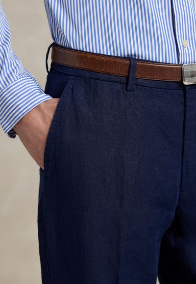 Marineblå linbukser med en slank passform, utstyrt med et brunt lærbelte og lyseblå stripete skjortearmer synlige ved ermene.