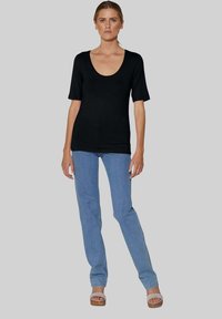 Schwarzes kurzärmeliges Oberteil mit Rundhalsausschnitt, kombiniert mit hellblauen geraden Jeans und sandfarbenen Plateau-Sandalen. Glatte Textur, lässige Passform.