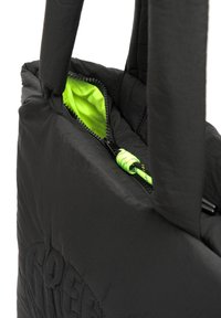 Sac fourre-tout noir matelassé avec fermeture à glissière, intérieur vert néon et fermeture à cordon. Matériau texturé et poignées robustes.