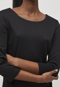 Svart långärmad topp med rund halsringning och mjuk textur. Har ärmar som når till armbågen och en avslappnad passform, lämplig för olika tillfällen.