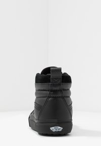 Černé vysoké tenisky vyrobené z kůže a semiše s polstrovaným límcem, texturovaným povrchem a bílou gumovou podrážkou. Na patě se nachází logo Vans.