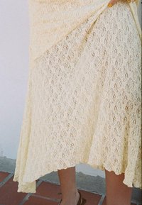 Jupe en dentelle crème jusqu'aux genoux avec motif floral et ourlet en forme de scallop. Le tissu a une apparence texturée avec des éléments de design superposés.
