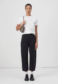 White t-shirt with pink text, high-waisted black wide-leg jeans, white socks, black chunky shoes, and a small gray handbag.