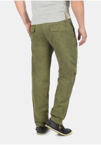 Olive green cotton pants with a relaxed fit, featuring two back pockets and a button detail, paired with dark footwear.
