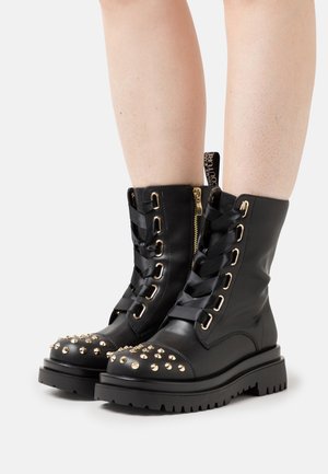 Mustat nahkaiset taistelukengät, joissa on kultaiset yksityiskohdat, nauhakiinnitys edessä, niittiyksityiskohta varpaassa ja sivuvetoketju helppoa käyttöä varten. Texturoitu kumipohja.