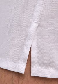 Tissu blanc à motif chevron, avec une fente latérale et des coutures nettes le long de l'ourlet, mettant en valeur une texture et un design lisses.