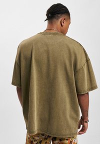 Olive green oversized T-shirt made from soft cotton; features short sleeves, a round neckline, and visible stitching details.
