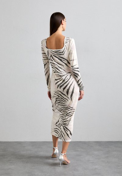 Dlhé rukávy, priliehavé šaty v krémovej farbe s čiernymi pruhmi zebra. Majú štvrtý výstrih na chrbte a dĺžku po polovicu lýtok.Čo sa týka obuvi, nosia sa k nim strieborné podpätky.