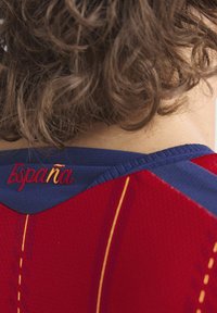 Maillot rouge et bleu avec un tissu texturé. "Espagne" est brodé en rouge dans la zone du cou à l'arrière, avec des lignes d'accent jaune.