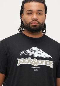 Μαύρο βαμβακερό t-shirt με λευκό γραφικό βουνού και λογότυπο "jack & jones" σε ασημί. Κλασικός στρογγυλός γιακάς και κοντά μανίκια.