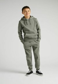 Grå hættetrøje med kængurulomme, parret med matchende joggers. Har en afslappet pasform og ribbede manchetter. Sorte sneakers med hvide accenter.