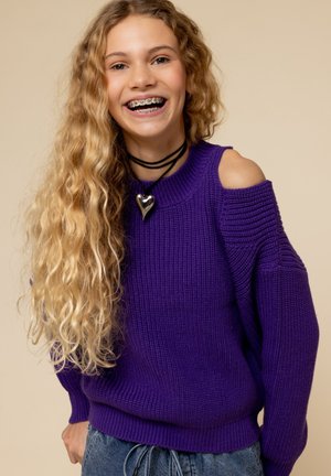 Paarse gebreide trui met een cold shoulder ontwerp, geribbeld textuur en een relaxte pasvorm. Draag een zwarte choker en blauwe jeans.