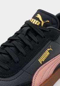 Sneaker in pelle nera con dettagli rosa, linguetta testurizzata, logo dorato e lacci neri. Presenta un colletto imbottito e una suola in gomma.