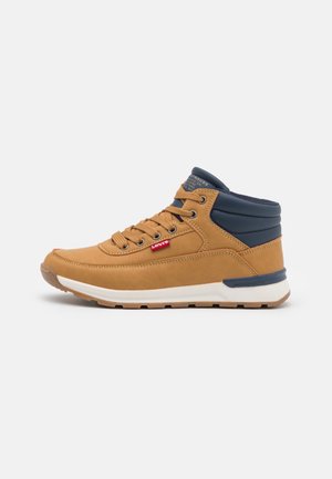 Brun og marineblå midt-høj sneaker med hvid sål, brune snørebånd og rød Levi's logo label på siden.